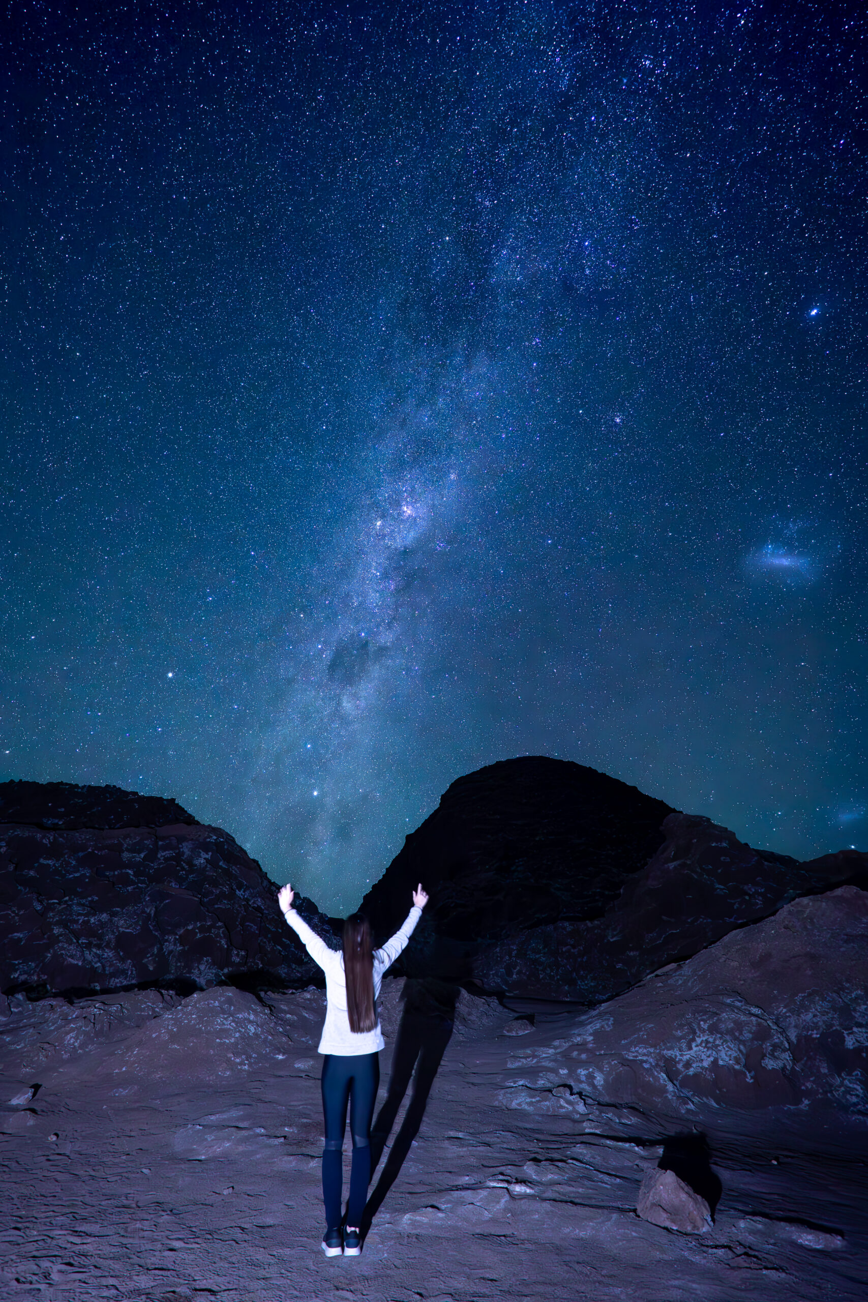 astrofotografía en la cordillera de la sal donde se ve a una chica de espaldas contemplando el cielo estrellado rente a las dunas y formaciones rocosas de la cordillera de la sal, San Pedro de Atacama.