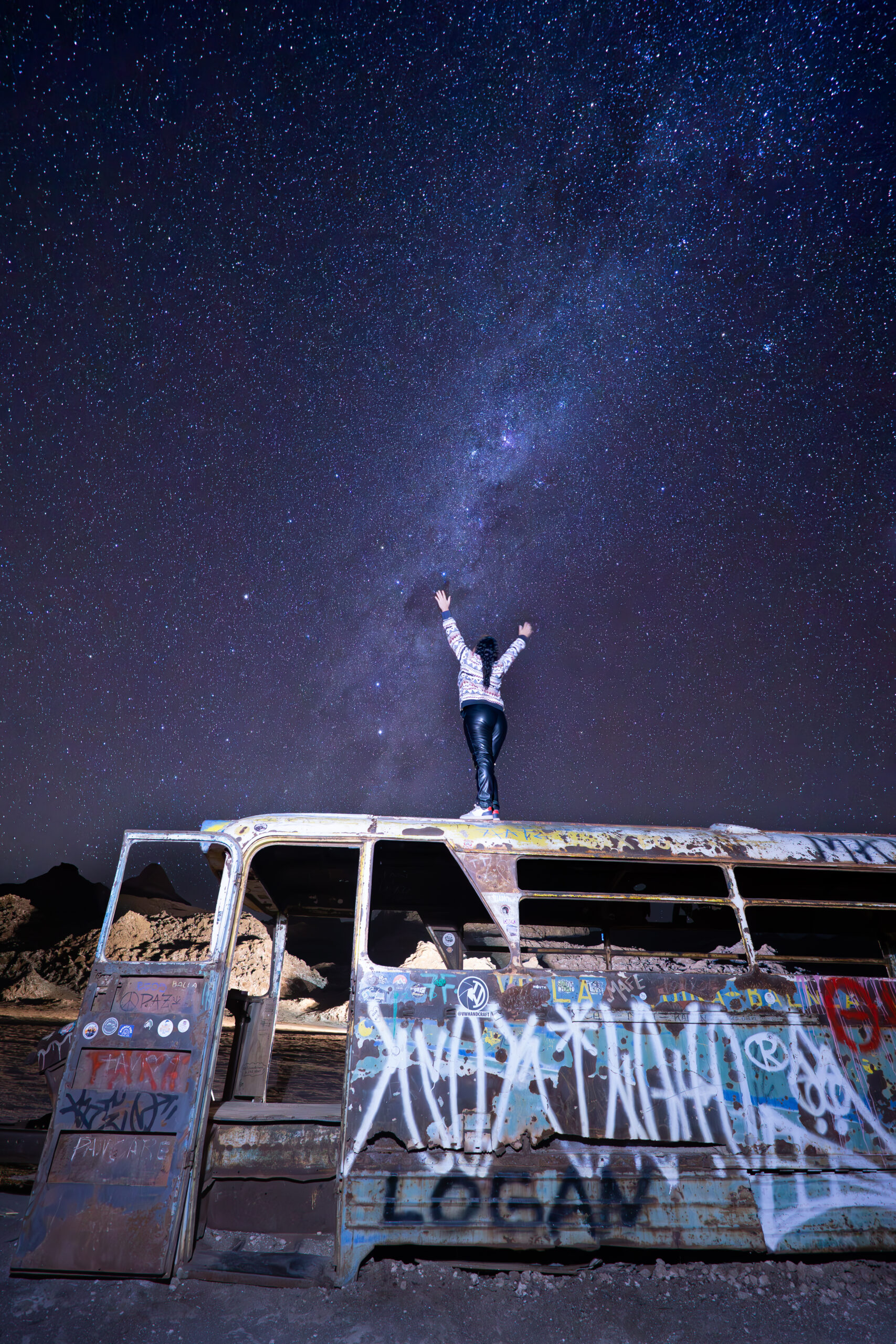 astrofotografía de una chica de espaldas encima del Bus Magico, bajo un manto de estrellas espectacular. Cordillera de la sal, san pedro de atacama.