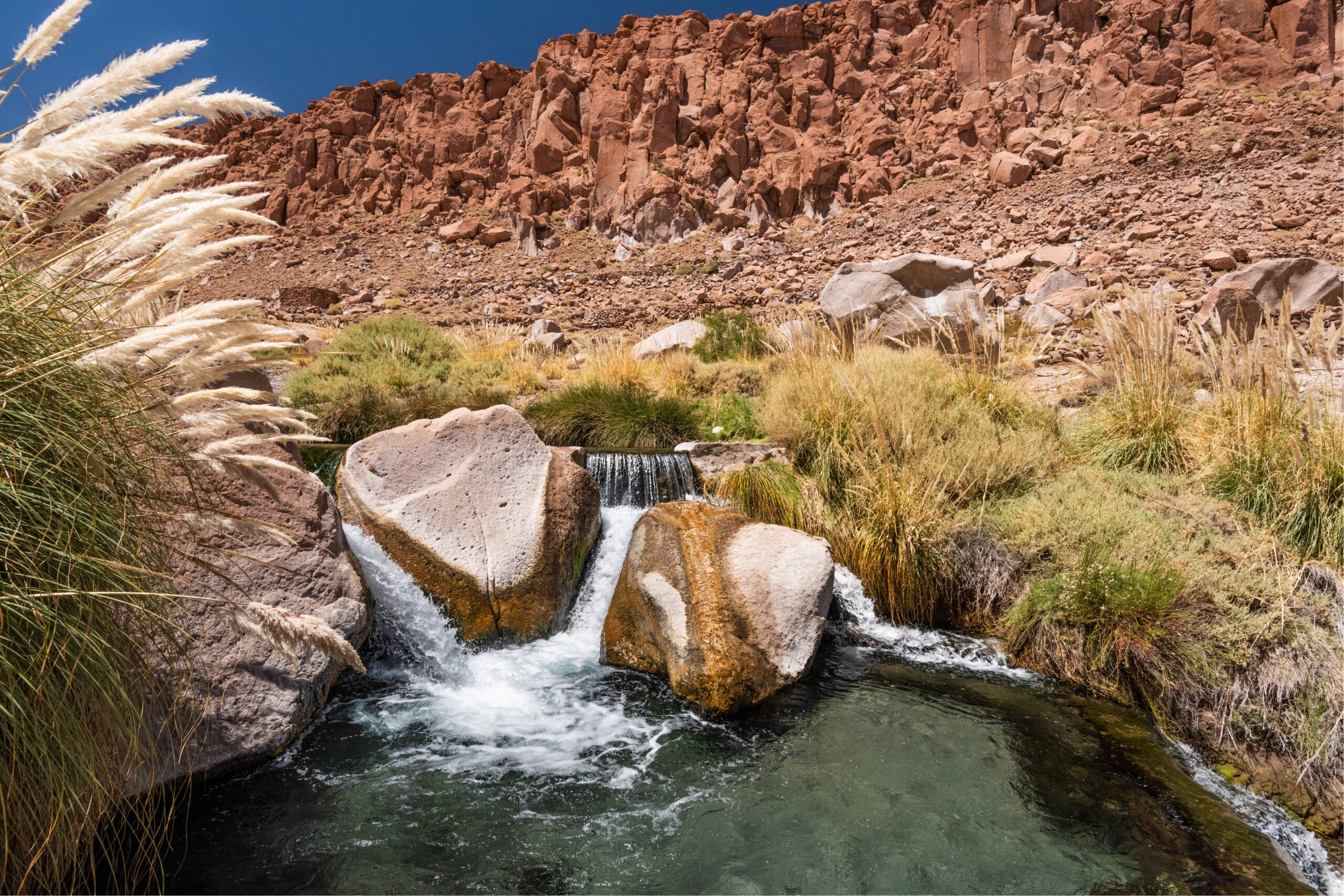 Fotografía del río Puritama formando una poza con grandes rocas y aguas termales donde relajarse. Termas de Puritama, San Pedro de Atacama.