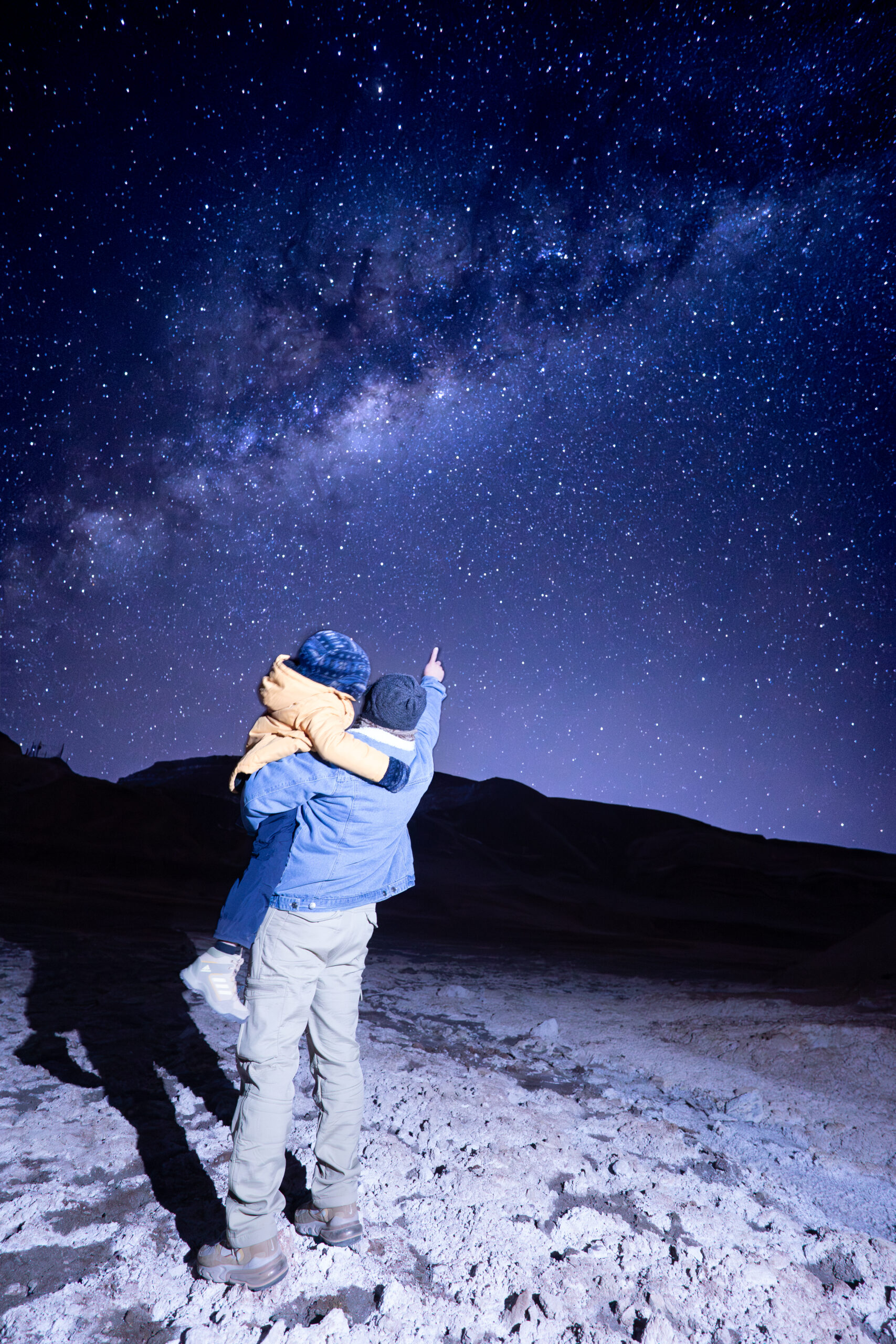 astrofotografía en la cordillera de la sal donde se ve a una chica de espaldas contemplando el cielo estrellado rente a las dunas y formaciones rocosas de la cordillera de la sal, San Pedro de Atacama.